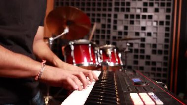 Modern stüdyoda, davul setinde ve arka planda ses geçirmez duvarda müzik provası yaparken Asyalı bir adamın elektronik klavye çalışını yakın plan.