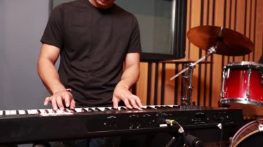 Asyalı müzisyen ellerinin dijital klavye çaldığı yakın plan, arka planda kırmızı davullar, bir stüdyo reçelinde duygu ve hareketi yakalamak