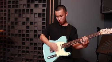 İki Asyalı adam, açık mavi elektro gitar ve kırmızı davullarla birlikte stüdyo ortamında, enerjik grup çalışması yapıyorlar.