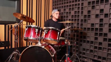 Asyalı davulcu, müzik prova stüdyosunda solo performans sergiliyor odaklanmış ifade ve dinamik hareket kaydedildi.