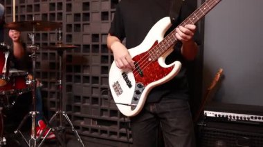 Profesyonel bir stüdyoda üç Asyalı genç adam canlı prova sırasında bateri, gitar ve klavye çalıyor.