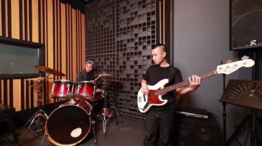 Profesyonel ses geçirmez müzik stüdyosundaki prova sırasında birlikte bas gitar, klavye ve davul çalan üç Asyalı genç müzisyen ritim ve takım çalışmasına odaklandı.