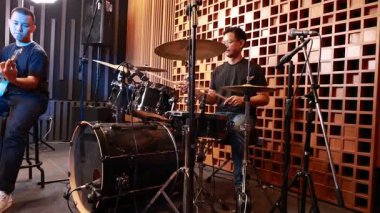 Profesyonel ses geçirmez stüdyoda elektro gitar ve davul çalan iki genç Asyalı erkek müzisyen, kayıt ekipmanlarıyla çevrili canlı performans oturumuna derinden odaklandılar.