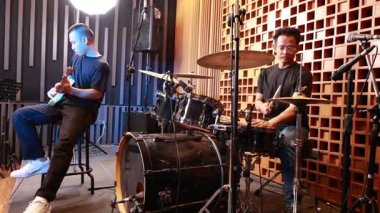 Profesyonel ses geçirmez stüdyoda elektro gitar ve davul çalan iki genç Asyalı erkek müzisyen canlı performans oturumunda birlikte çalışıyorlar.