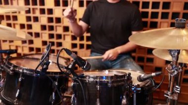 Genç Asyalı erkek davulcu elleri, kayıt stüdyosundaki davul setinde, mikrofon kurulumunu ve çalma tekniğini gösteren bagetlerle yakın çekim.