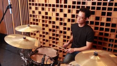 Genç Asyalı erkek davulcunun profesyonel stüdyoda müzik seansı sırasında sessiz zillerde baget kullanarak performans sergilemesini izlemek.