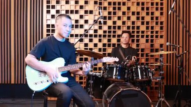 Profesyonel kayıt stüdyosunda elektro gitar ve davul çalan iki genç Asyalı erkek müzisyen, performansa odaklanmış, birlikte ritim ve uyum yaratmaya çalışmışlardır.