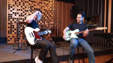 İki genç erkek müzisyen, müzik seansını beşlikle kutlarken stüdyoda elektro gitar ve bas tutarak başarı ve dostluğu ifade ediyorlar.