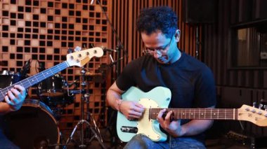 Akustik stüdyoda elektro gitar ve bas çalan iki erkek müzisyenin sahnesi. Kamera gitaristten basçıya sorunsuzca çekiliyor. Odaklanma ve işbirliği gösteriyor.