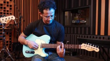 Profesyonel akustik stüdyoda açık mavi gitar çalan erkek müzisyen, müzik oluşturma ortamında konsantrasyon ve tutku gösteriyor