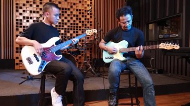 İki erkek müzisyen profesyonel akustik kayıt stüdyosunda birlikte performans sergiliyorlar, biri bas gitar çalıyor, diğeri elektro gitar çalıyor, odaklanmış ve yaratıcı atmosfer.