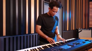 Siyah tişörtlü Asyalı adam kontrol düğmeleri ve ses geçirmez müzik stüdyosundaki elektrikli klavyenin düğmeleri, ses ayarlarını konsantrasyon ve modern kapalı ortam ile ayarlıyor.