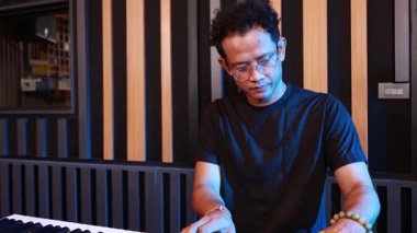 Kayıt stüdyosunda elektronik klavye çalan genç Asyalı erkek müzisyen, müzik pratiği sırasında sakin ve odaklanmış, akustik duvar arka planına sahip kapalı alanda ışıklandırma