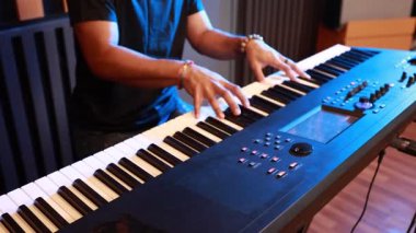 Profesyonel müzik stüdyosunda Asyalı bir adamın ellerinin elektronik klavye çalmasının ayrıntıları geniş açıda modern akustik panellerle ses geçirmez odada müzisyen performansı sergiliyor.