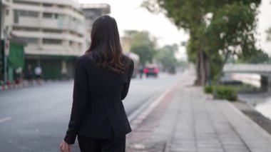 Kentte gündüz haberleri sunarken kentin kaldırımlarında yürüyen, konuşan ve kameraya gülümseyen resmi takım elbiseli kendine güvenen Asyalı kadın gazeteci.