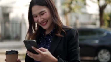 Asyalı iş kadını elinde kahve ve akıllı telefonuyla, gülümseyerek müzik dinlerken kamera onun etrafında dönüyor, neşeli bir ruh hali ve kendine güvenen bir yaşam tarzı sergiliyor.