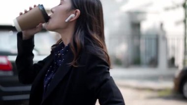 Asyalı iş kadını kahve içerken ve müzik dinlerken gülümsüyor, kablosuz kulaklık takıyor, farklı açıları gösteren bir kamera, kentsel yaşam tarzında huzurlu bir an.