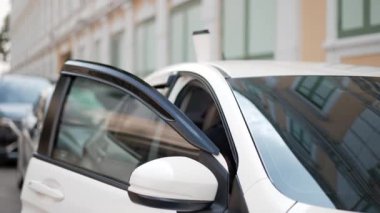 Genç Asyalı bir kadın park halindeki bir arabanın yanında beklerken cep telefonundan birini arıyor, sonra da arkadaşının şehir ortamında yaklaştığını görünce heyecanla el sallıyor.