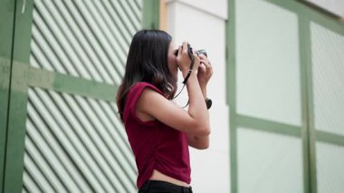 Dijital kamera, günlük kıyafet ve sakin atmosfer, yaşam tarzı ve seyahat konseptiyle şehir sahnesini fotoğraflayan Asyalı genç kadının yan görüntüsü