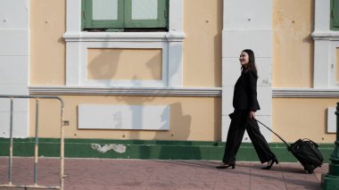 Asyalı kadın profesyonel elinde kağıt kahve fincanı ve akıllı telefon ile şehir sokaklarında koşuyor, aciliyet ve odaklanmış ifade gösteriyor, çoklu görevi temsil ediyor, teslim süresi baskısı ve şehir ortamında modern iş yaşam tarzını temsil ediyor
