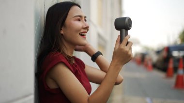 Neşeli Asyalı kadın, elinde taşınabilir bir yelpaze tutarken gülüyor. Günlük kırmızı kıyafetler ve şık kıyafetler giyiyor. Yaz tazeliğini, özgüvenini, özgüvenini ve enerjisini gösteriyor.