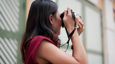 Genç Asyalı bir kadın dijital kamerayla fotoğraf çekerken yaratıcı bir açık hava ortamında vizör aracılığıyla fotoğrafçılık ve görsel hikaye anlatımına olan tutkusunu gösteriyor..