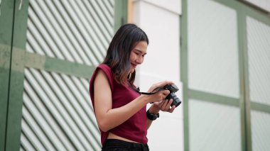 Genç Asyalı kadın dışarıda dijital kamerada fotoğrafları incelerken gülümsüyor, günlük ve yaratıcı bir anda fotoğraf için neşeli duygu ve tutku ifade ediyor..