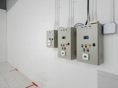 Elektrik tesisatı, mühendislik sistemi veya endüstriyel bakım için ideal, elektrik tesisatı, elektrik tesisatı ve fayanslı zemini olan beyaz duvardaki üç elektrik kontrol panelinin açılı görüntüsü.