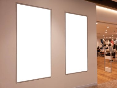 Alışveriş merkezindeki moda mağazası girişinin duvarında iki tane dikey boş reklam panosu var. Ilık ışıklandırma ve arka planı var. Perakende reklamı, poster tasarımı veya marka tanıtımı için mükemmel.