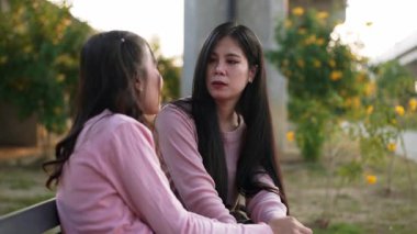 İki genç Asyalı kadın parkta bankta oturuyor, biri diğerinin duygusal görünmesine yardım ediyor. Tartışma sırasında el ele tutuşuyorlar. Bir destek ve dostluk anı..