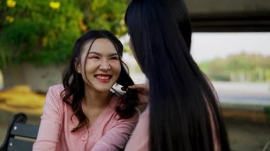 İki genç Asyalı kadın parkta bankta oturuyor, biri diğerinin duygusal görünmesine yardım ediyor. Tartışma sırasında el ele tutuşuyorlar. Bir destek ve dostluk anı..