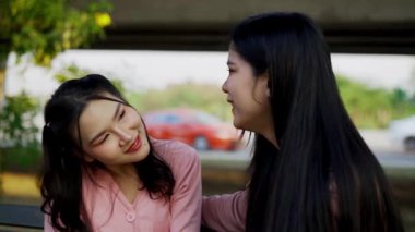 İki genç Asyalı kadın parkta bankta oturuyor, biri diğerinin duygusal görünmesine yardım ediyor. Tartışma sırasında el ele tutuşuyorlar. Bir destek ve dostluk anı..