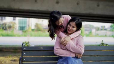İki genç Asyalı kadın parkta bankta oturuyor, biri diğerinin duygusal görünmesine yardım ediyor. Tartışma sırasında el ele tutuşuyorlar. Bir destek ve dostluk anı..