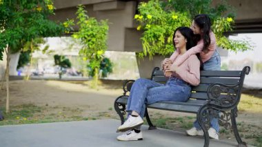 İki genç Asyalı kadın parkta bankta oturuyor, biri diğerinin duygusal görünmesine yardım ediyor. Tartışma sırasında el ele tutuşuyorlar. Bir destek ve dostluk anı..