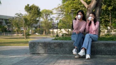 İki genç Asyalı kadın parkta bankta oturuyor, biri diğerinin duygusal görünmesine yardım ediyor. Tartışma sırasında el ele tutuşuyorlar. Bir destek ve dostluk anı..