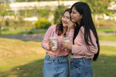 Büyüleyici genç lezbiyen çift dışarıda neşeli anları paylaşıyor. Kamu parkında buzlu kahve içiyorlar. İçten ve sevgi dolu bir an. Doğanın güzelliğiyle çevrili.