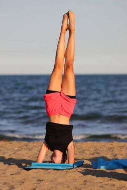 Genç kız yaz aylarında deniz kenarında egzersiz yaparken spor minderinde dengede duruyor.