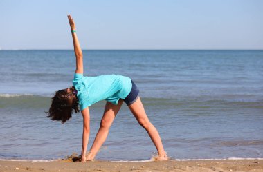 Genç kız deniz kenarında jimnastik yaparken