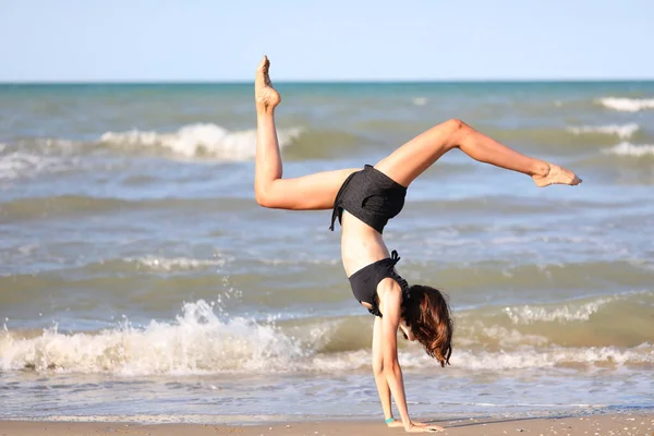 穿着黑色泳衣的年轻赤脚姑娘在海滨进行有节奏的体操锻炼 — 图库照片