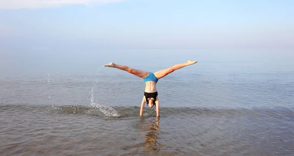 若い女の子は夏に海岸で逆さまの頭で体操をします — ストック写真