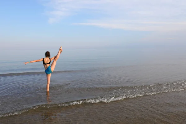 Smukła Atletyczna Dziewczyna Wykonuje Ćwiczenia Gimnastyczne Morzu Pobliżu Brzegu Latem — Zdjęcie stockowe