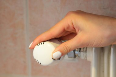 Enerji tasarrufu için radyatörlerin sıcaklığını ayarlamak için beyaz termostatik vanayı düzenleyen el.