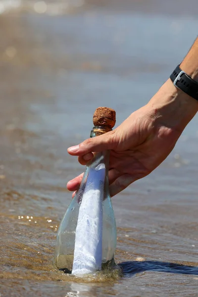 hand picking up glass bottle with message inside from sea