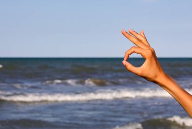 hand of girl making OK symbol by the sea in summer