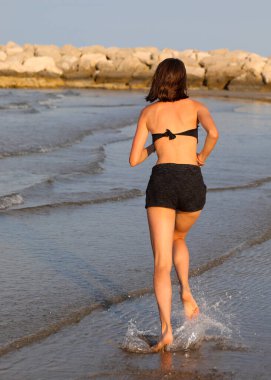 Genç kız yazın plajda mayoyla koşuyor.