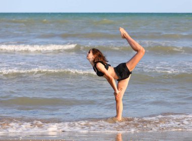Kız yazın deniz kenarındaki kumsalda jimnastik yapıyor.