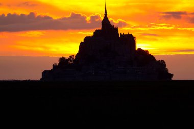 red sky with clouds at sunset and the silhouette of the Mont Saint Michel abbey in Northern France