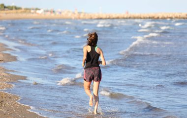 Yazın antrenman yapmak için sahilde koşan atletik kız.