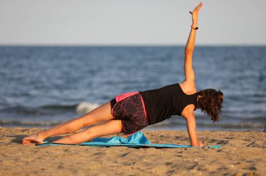 young girl training by the sea in summer on the gym mat on the beach at sunset