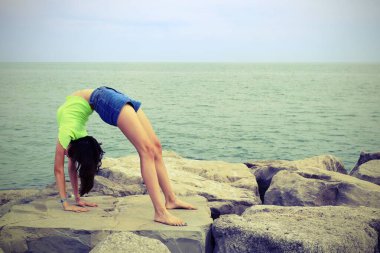 Genç kız deniz kenarındaki kayalıklarda antika tonlama efektiyle jimnastik yapıyor.